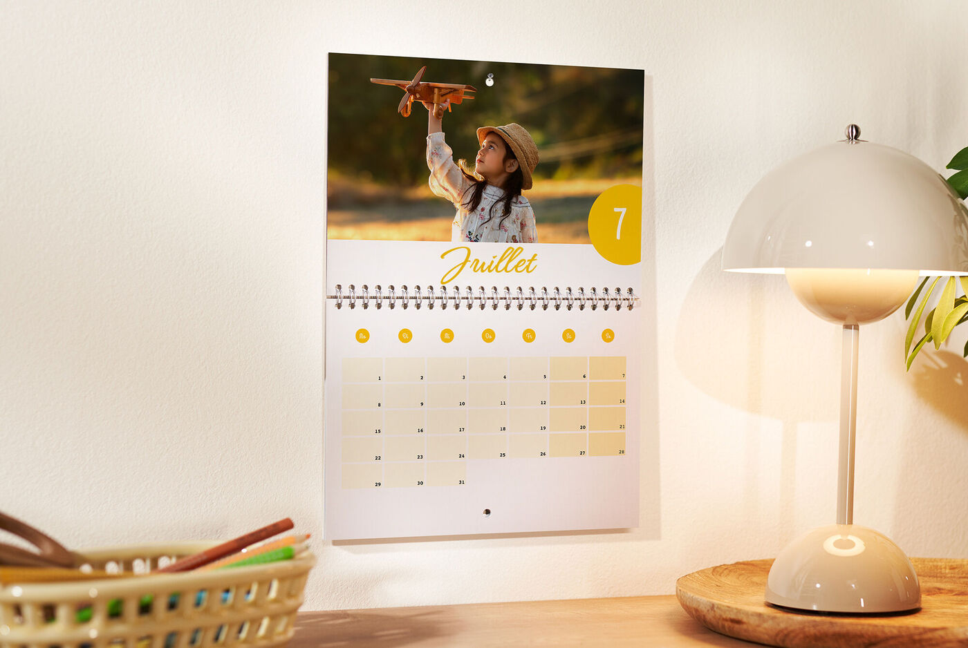Un calendrier mural montre un enfant joyeux tenant un avion jouet. Juillet est en surbrillance.