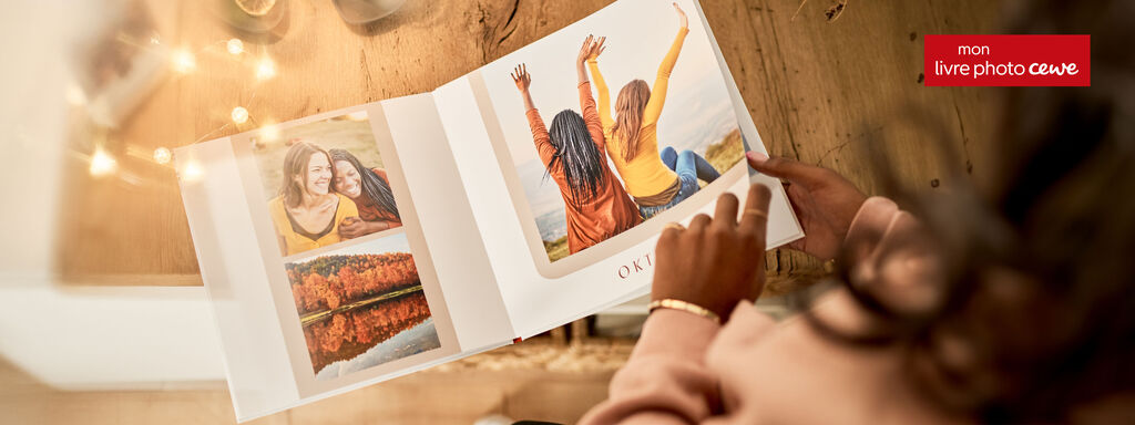 Quelqu'un feuillette un PRODUIT PHOTO CEWE contenant des photos d'amis autour d'une table conviviale.